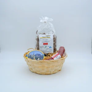 Geflochtener Präsentkorb mit typisch bündnerischen Produkten: Gran Alpin Pizzoccheri, eine kleine Bündner Nusstorte und ein Salsiz der Metzgerei Sialm, arrangiert auf Holzwolle vor weissem Studiohintergrund